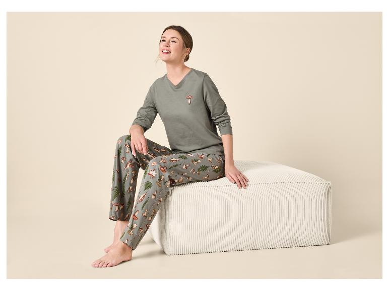 Vrouw in pyjama met paddenstoelprint zit op een witte poef, kijkt omhoog en lacht.