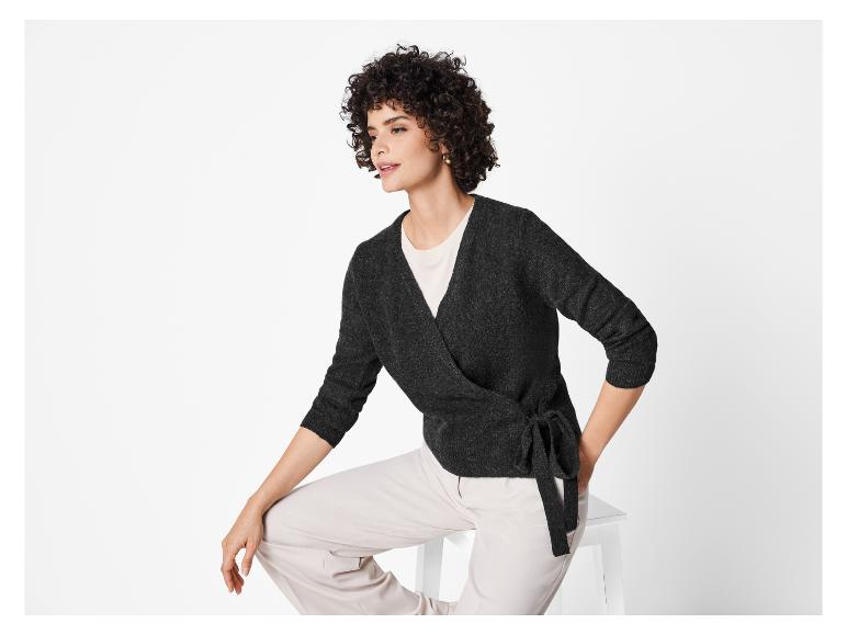 Een vrouw draagt een donkergrijze trui en beige broek.