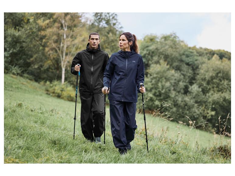 Twee mensen lopen in regenkleding en met wandelstokken door een weiland.