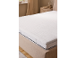 Witte matrastopper op een bed in een neutraal getinte slaapkamer.
