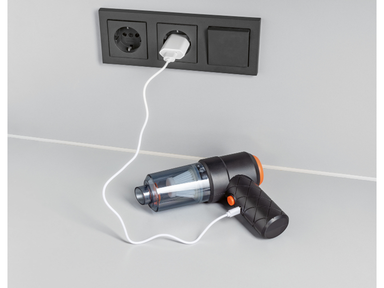 Handstofzuiger laadt op via een stopcontact aan de muur op een lichtgrijze ondergrond.