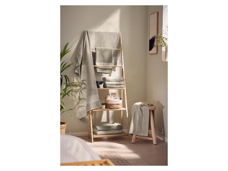 Badkamerinterieur met houten ladderrek en groene handdoeken.