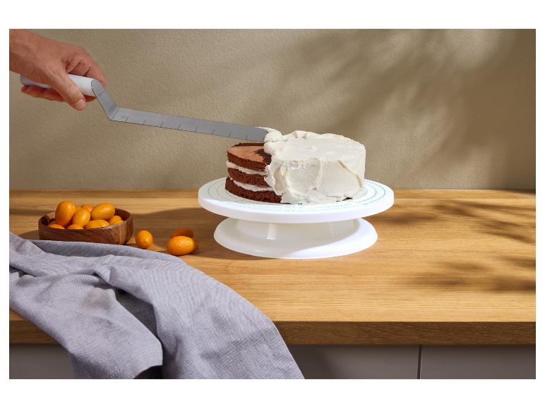 Hand glazuurt een chocoladetaart op een draaiplateau, met kumquats en een grijze doek ernaast.