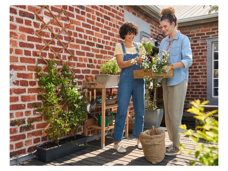 Twee vrouwen planten bloemen in een plantenbak op een houten terras.
