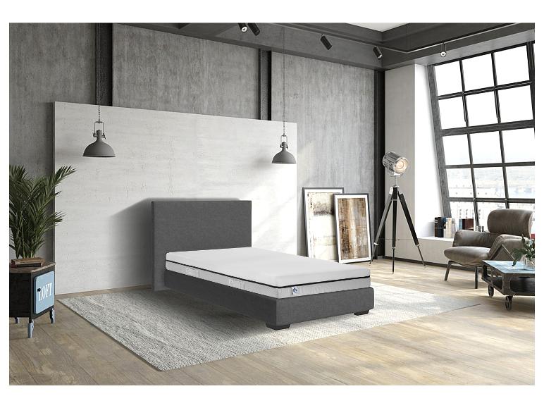 Een grijs bedframe met een witte matras in een moderne slaapkamer.