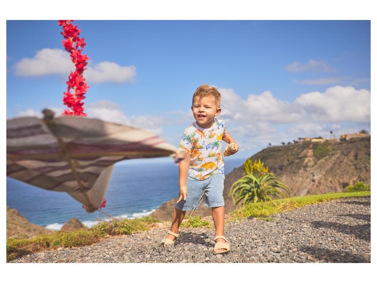 Jongen in dinosaurus T-shirt en korte broek speelt aan de kust.