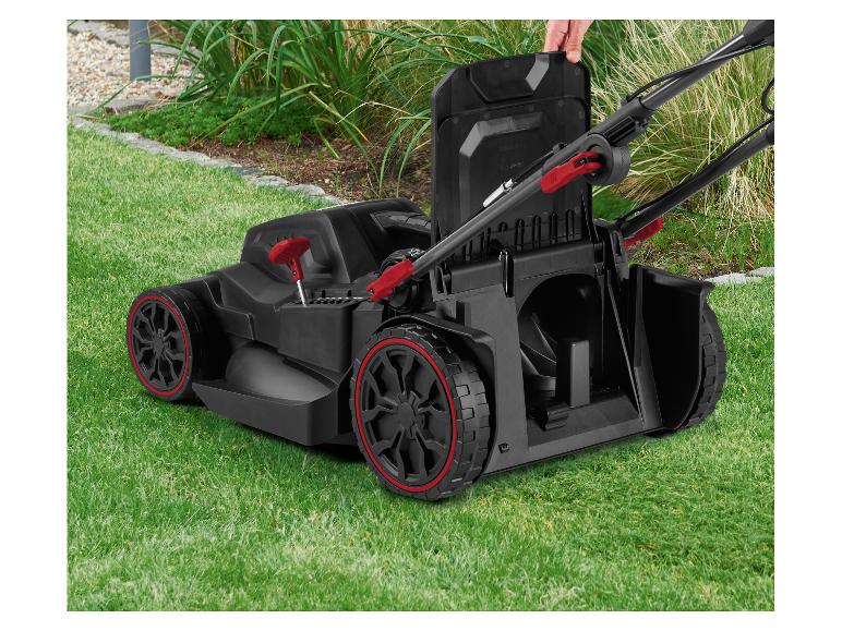 Accu grasmaaier met rode accenten op groen gras, een hand opent de bovenklep.