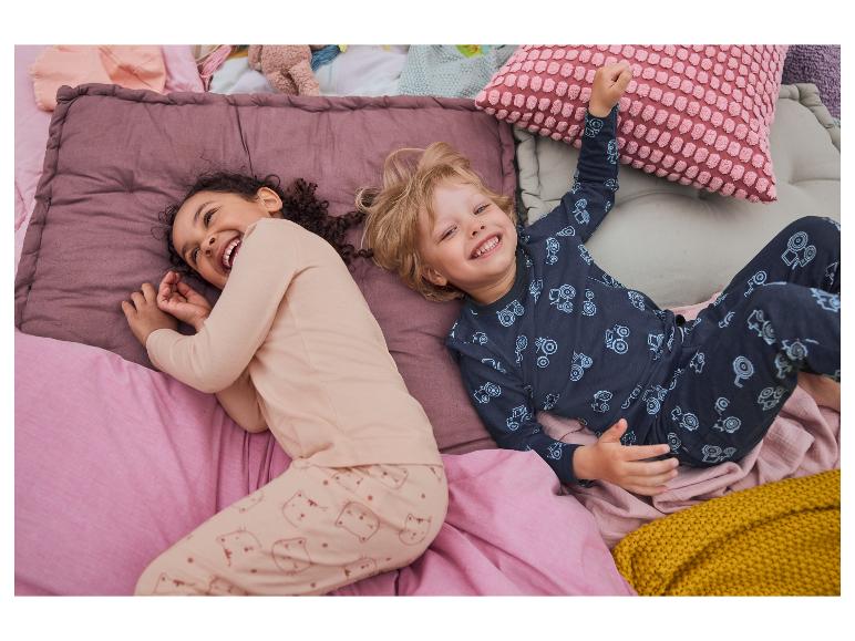 Kinderen lachen in bed met pastelkleurige beddengoed met katten- en tractorprints.