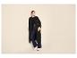 Vrouw in zwarte trenchcoat, wide-leg jeans en witte sneakers.