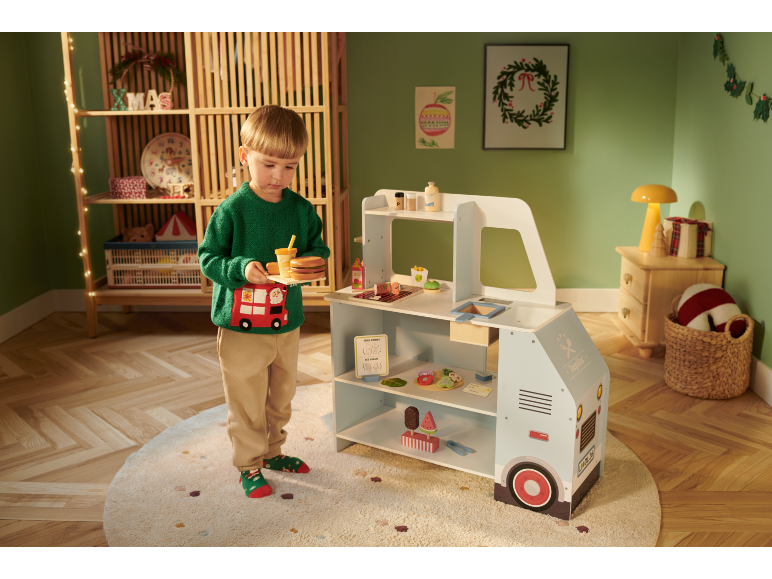Een jongen speelt met een houten speelgoedfoodtruck in een feestelijk versierde kamer.
