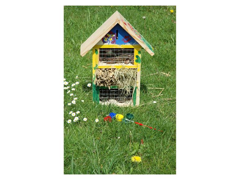 Kleurrijk houten insectenhotel in gras met madeliefjes en paardenbloemen.