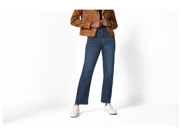 Persoon draagt een bruine suède jas, donkerblauwe jeans en witte sneakers.