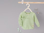 Een lichtgroen baby shirt met lange mouwen, hangend aan een houten hanger.