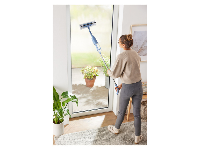 Een vrouw gebruikt een Vileda-raamwisser om een raam schoon te maken.