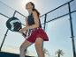 Vrouw in sportkleding met padelracket op de baan, lachend en omhoogkijkend.