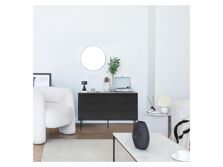 Zwarte ladekast, ronde spiegel, witte fauteuil en platenspeler in een woonkamer.