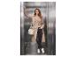 Vrouw in beige trenchcoat, zwarte broek en witte sneakers met tas in lift.