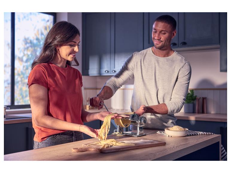 Koppel maakt verse pasta met pastamachine in een moderne keuken.