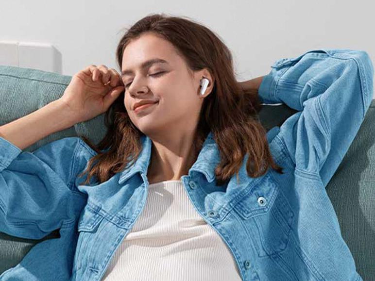 Vrouw ontspant op een bank, luisterend naar muziek met witte in-ear koptelefoons.