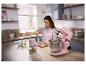 Vrouw in de keuken bereidt maaltijd met roze keukenmachine en hakmolen.