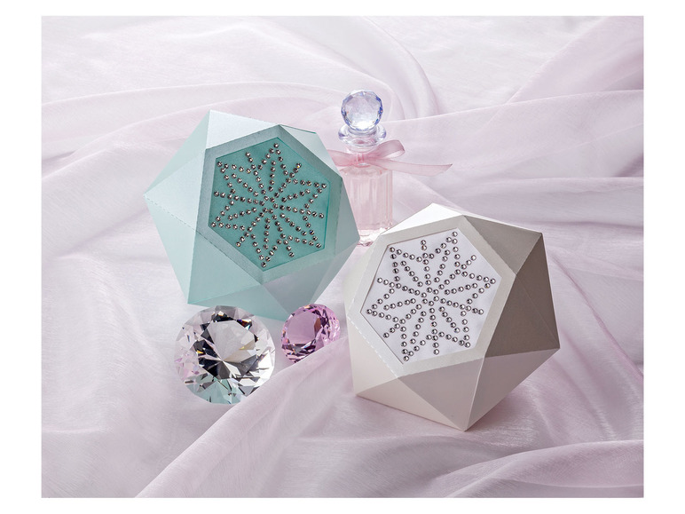 Twee doosjes met sneeuwvlokken en een flesje parfum op een roze doek.