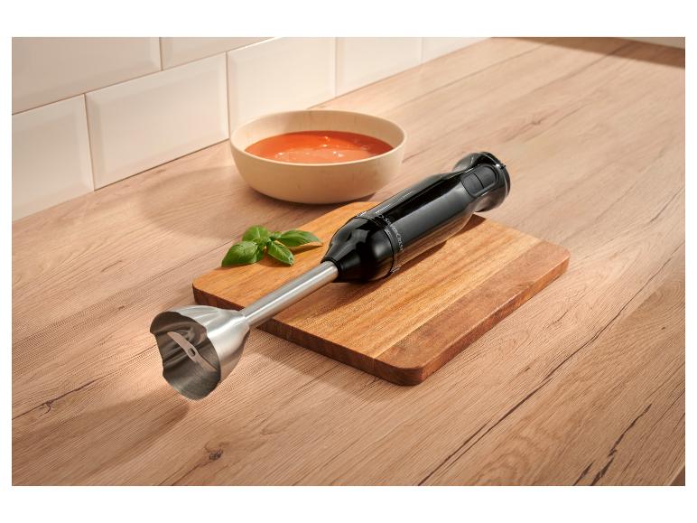Zwarte staafmixer op een houten snijplank naast een kom tomatensoep.