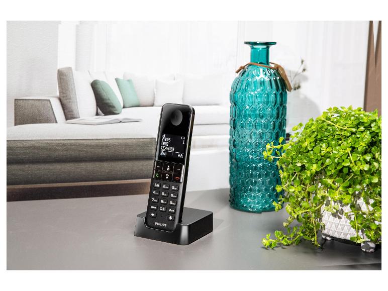 Draadloze telefoon met oplaadstation op tafel, naast een vaas en plant.
