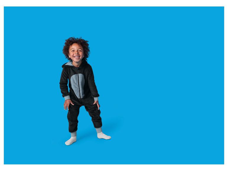 Een lachend kind draagt een zwarte pluizige onesie met een grijze buik.