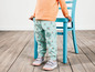 Een kind draagt een roze shirt en blauwe broek met bloemenprint.