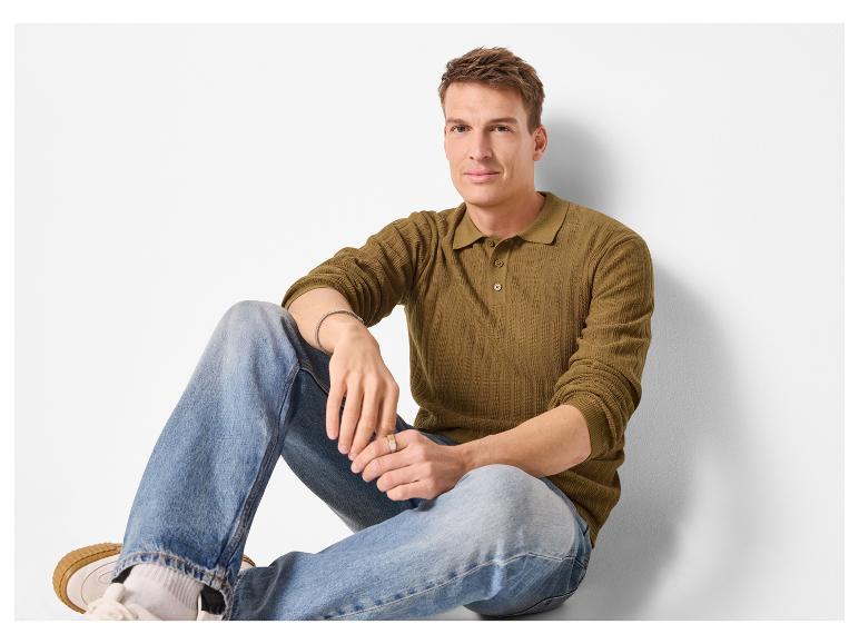 Man in een groen poloshirt met lange mouwen en blauwe jeans zit op de grond.