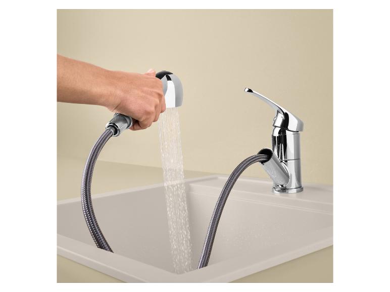 Keukenkraan met uittrekbare sproeier in een beige spoelbak, met stromend water.