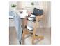 Verstelbare houten kinderstoel met een grijze zitting en voetensteun, naast een witte tafel.