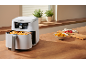 Witte airfryer met frietjes en een kom met kipnuggets op een houten tafel.