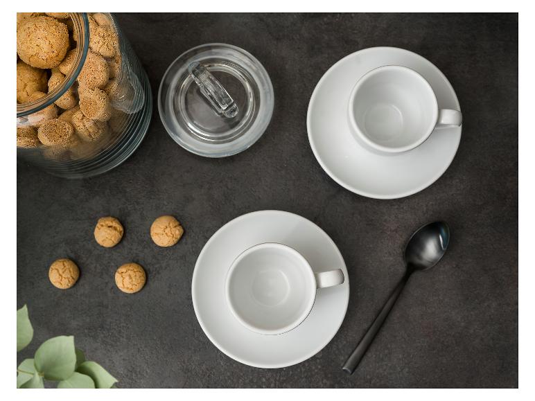 Bovenaanzicht van een glazen pot met amaretti koekjes, twee lege espressokopjes en een lepel.