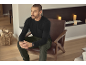 Man in zwart shirt met lange mouwen en groene broek zit in een leren stoel.