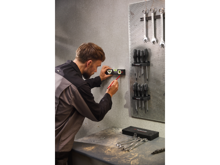 Man gebruikt waterpas en potlood om een punt op de muur in een werkplaats te markeren.