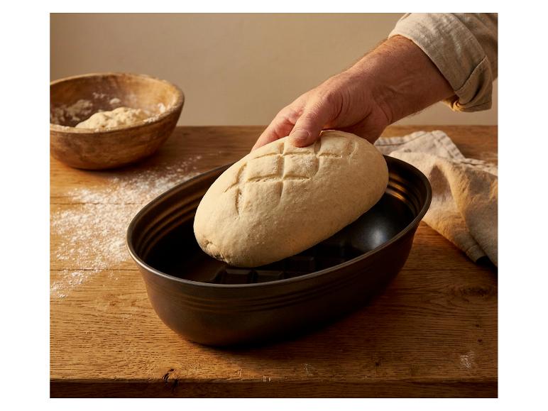 Hand plaatst brooddeeg in een ovale bakvorm op een houten tafel.