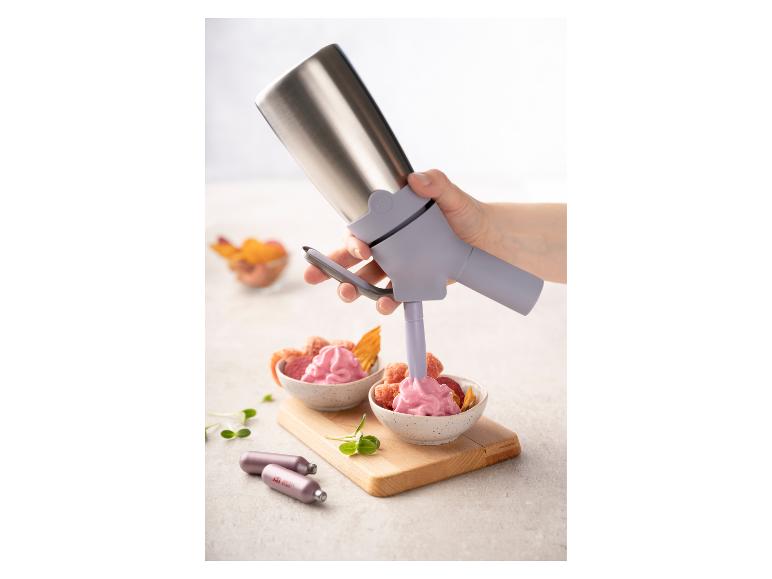 Een hand gebruikt een slagroomdispenser om een kom met roze schuim te vullen.