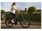 Jonge vrouw in spijkerjack en donkere jeans rijdt op een e-bike door een woonstraat.