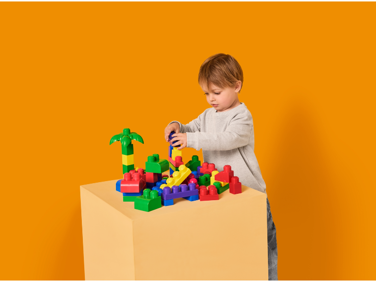 Een jonge jongen speelt met kleurrijke bouwstenen op een tafel tegen een oranje achtergrond.