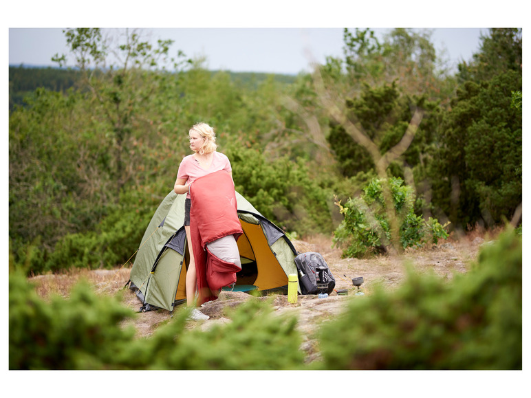 Een vrouw zet een slaapzak neer in een groene tent tijdens een kampeertrip.