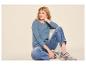 Vrouw in blauw T-shirt met lange mouwen, jeans en sneakers, zittend op de grond.