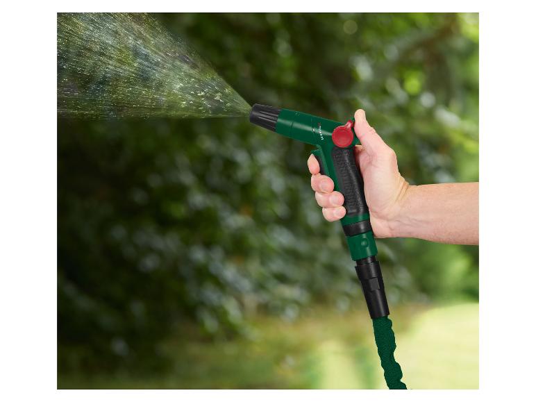Hand houdt een groene tuinspuit vast, die water sproeit tegen een weelderige groene achtergrond.