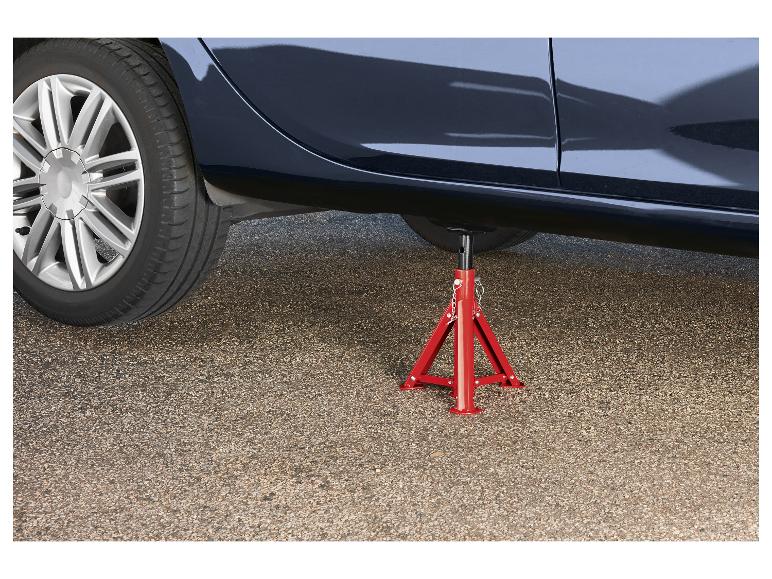 Een auto ondersteund door een rode assteun op een asfaltweg.