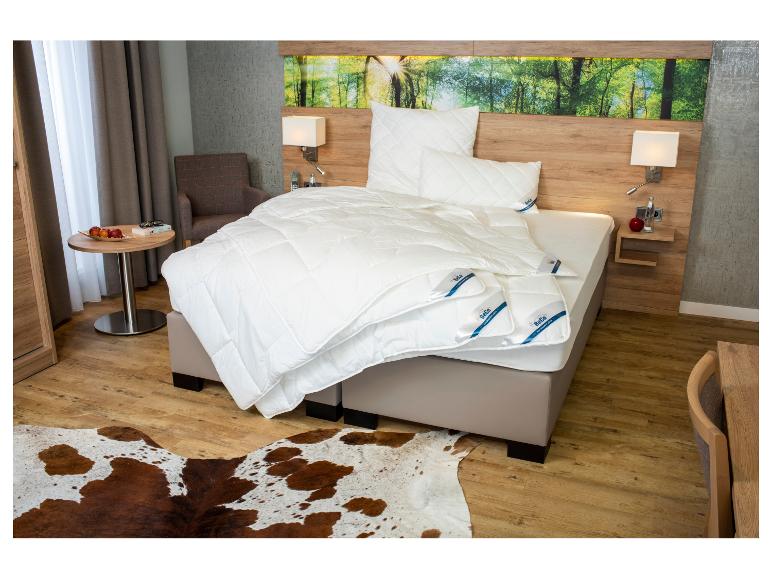 Moderne slaapkamer met bed, wit BeCo beddengoed, houten nachtkastjes en een koeienhuid vloerkleed.