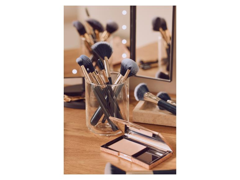 Make-upkwasten in een glazen houder en een compact poeder op een houten kaptafel.