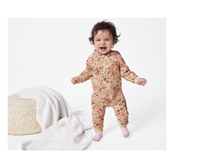 Lachende baby in een bloemen jumpsuit met capuchon.