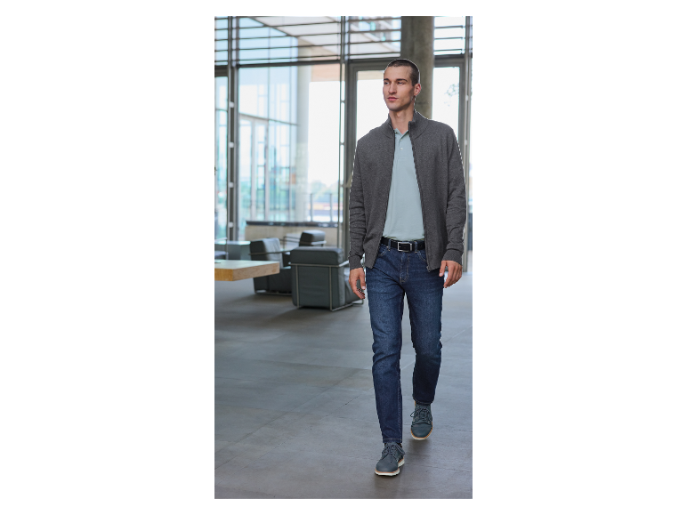 Een man in een grijze trui en jeans.