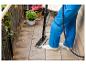 Persoon reinigt balkontegels met stoommop, met planten in potten ernaast.