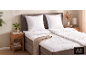 Bed met wit dekbed en kussens, houten nachtkastjes met planten en decoraties.